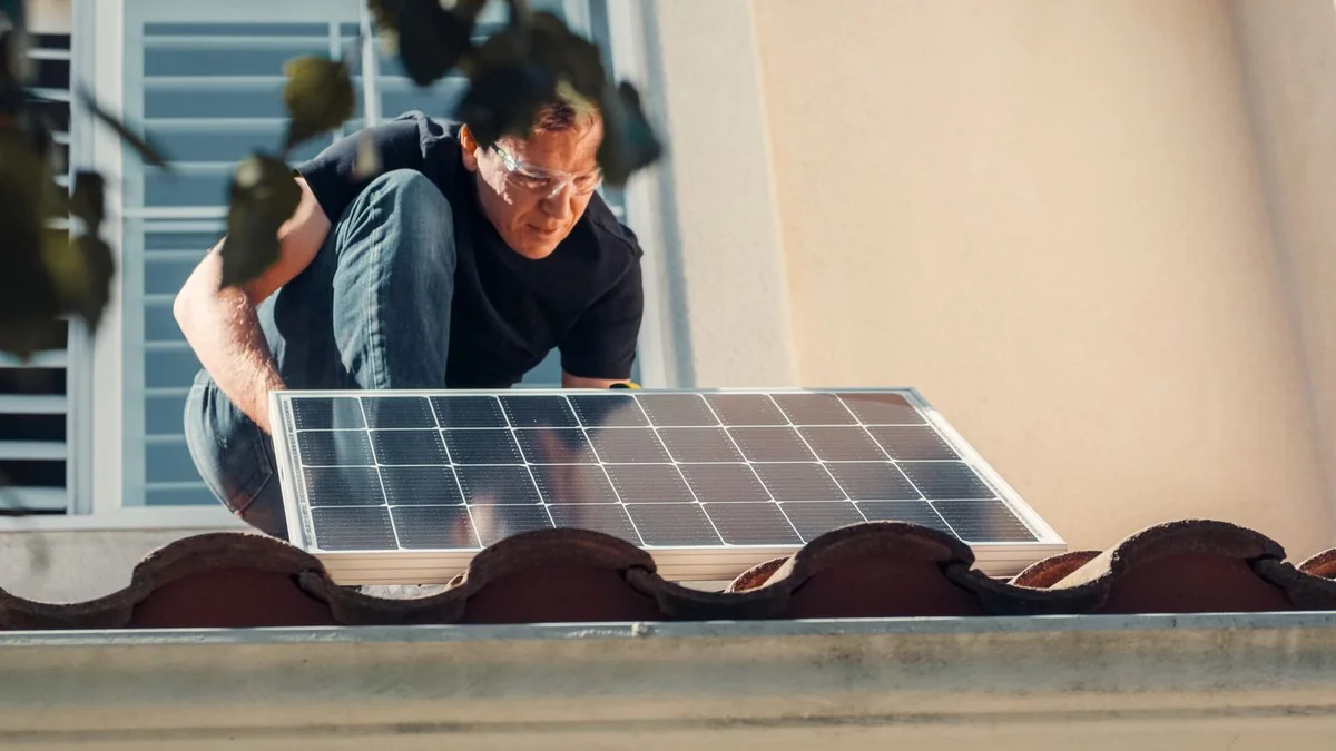 Instalator montând un panou fotovoltaic pe acoperișul unei case