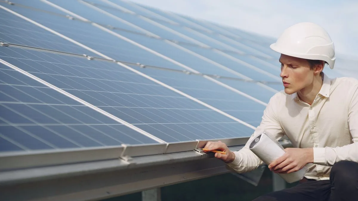Inginer cu cască de protecție care inspectează rama și prinderile panourilor fotovoltaice dintr-un parc solar