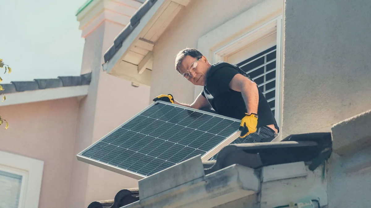 Instalator cu ochelari și mănuși de protecție care montează un panou fotovoltaic pe acoperiș