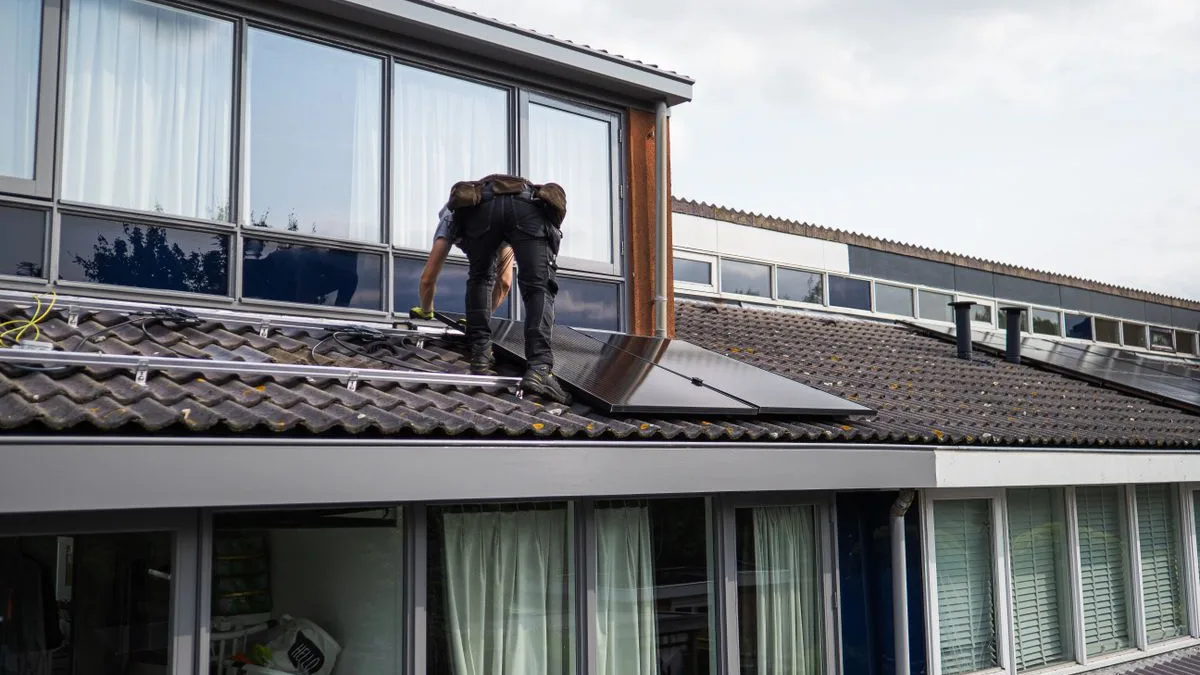 Instalator care montează panouri fotovoltaice pe șine fixate pe un acoperiș de țiglă